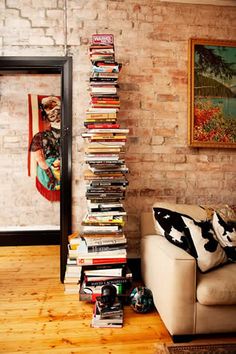 a stack of books sitting on top of a white couch in front of a brick wall