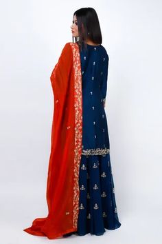 Navy blue kurta featuring zari embroidered floral motifs highlighted with sequin, cut dana and pearls. Comes with sharara and contrasting red dupatta.
Components: 3
Pattern: Embroidered
Type Of Work: Cut dana, Sequin, Zari
Neckline: Round
Sleeve Type: Three quarter
Fabric: Kurta: Slub Silk, Sharara: Georgette, Dupatta: Silk Organza
Color: Blue
Other Details: 
Attached lining
Elasticated waistband
Contrast neck panel
Embroidered pearl detail
Occasion: Mehendi and Haldi,Sangeet - Aza Fashions Sharara Set, Silk Organza, Embroidered Silk, Three Quarter, Floral Motif, Aza Fashion, Types Of Sleeves, Silk, Blue