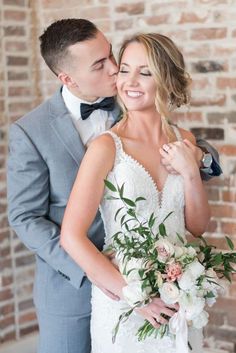 a bride and groom kissing in front of a brick wall at their wedding reception venue