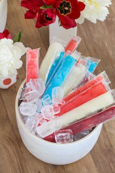 a bowl filled with different colored popsicles on top of a wooden table next to flowers