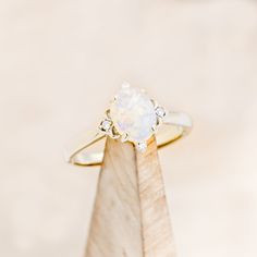 an opal and diamond ring sits on top of a piece of wood in front of a white background