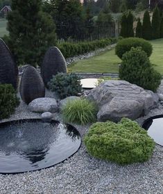 an outdoor pond surrounded by rocks and plants in the middle of a graveled area