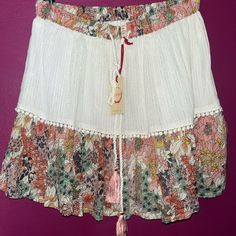 Raga Nwt Mini Skirt Love This It Has A Cream Too With Gold Strands Through The Material With A Floral Bottom. There Are Embellishments At The Fabric Split Line. Love! It Is The Gauze Material But Able Layered. Tassel Skirt For Summer, Tasseled Skirt For Summer, Bohemian Beach Skort (skirt Shorts), Bohemian Skirt-style Beach Shorts, Bohemian Skort For Beach, Summer Skirt With Tassels, Spring White Skirt With Tassels, White Tassel Skirt For Spring, Bohemian Fringe Mini Skirt For Summer