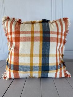 an orange and blue plaid pillow sitting on top of a wooden floor