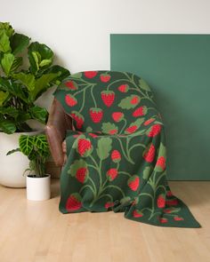 a chair covered in a green strawberry patterned blanket next to potted plants on the floor