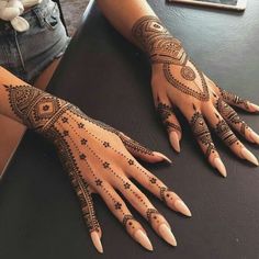 a woman's hand with henna tattoos on it, sitting at a table