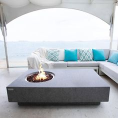 an outdoor fire pit with pillows on the couches and table in front of it