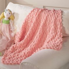 a pink crocheted blanket sitting on top of a couch next to a stuffed animal