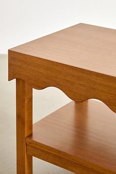 a small wooden table with one shelf on the top and two shelves below it, against a white wall