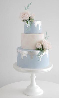 a three tiered cake with white flowers on the top and blue frosting around it