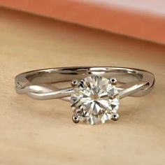 an engagement ring with a twisted band and a round diamond in the center on a wooden surface