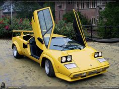 a yellow car with its doors open sitting on the ground in front of some bushes