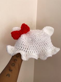 a hand holding a white crocheted teddy bear with a red bow on it