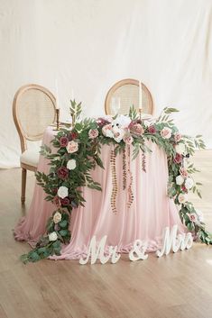 the table is covered with pink chiffon, greenery and mr and mrs signs