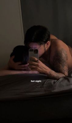 a shirtless man laying on a bed looking at his cell phone with the caption hot night