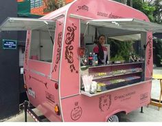 a pink food truck parked on the side of a road next to a building with a woman standing behind it