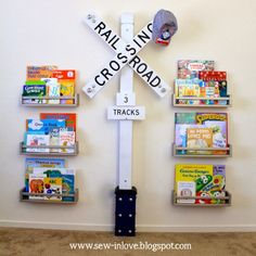 there is a sign that says rail crossing 3 tracks with books on the wall behind it