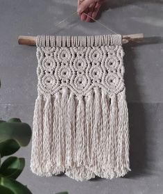 a person holding a piece of white yarn on a wooden hanger next to a potted plant