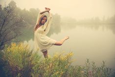 a woman standing on her legs in the air by a body of water with trees and bushes