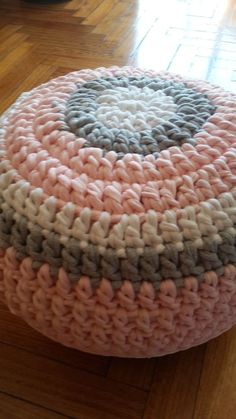 a pink and gray crocheted ottoman sitting on top of a hard wood floor