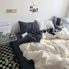 an unmade bed with white sheets and blue comforter next to a black and white checkered floor