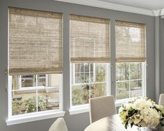 a dining room table with chairs and two windows covered in shades of light brown bamboo