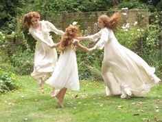 three women in white dresses are holding hands and running through the grass with their arms around each other