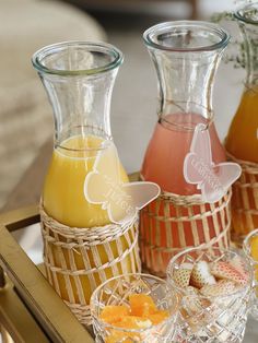 three vases filled with different types of liquid on top of a tray next to fruit