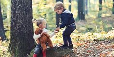 two young children playing with a teddy bear in the woods on a fall day,