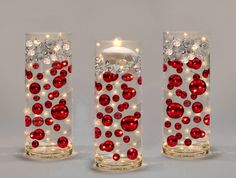 three glass vases with red and white ornaments on the sides, one holding a lit candle