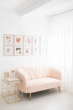 a living room with white walls and pink couch in front of the window, framed pictures on the wall