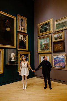 a man and woman holding hands in front of paintings