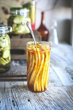 pickles and pickles in jars on a wooden table with spoon sticking out from one jar