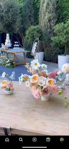 flowers in vases sitting on a wooden table outside with trees and bushes behind them