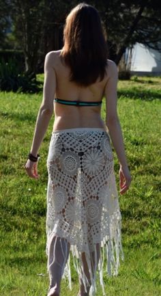 a woman in a white crochet skirt walking on the grass with her back to the camera