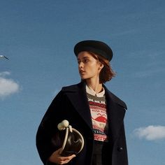 a woman in a black coat and hat is standing under a blue sky with two seagulls