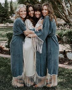 three women in robes hugging each other while standing on the grass with their arms around one another