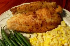 a white plate topped with chicken, corn and green beans on top of a wooden table