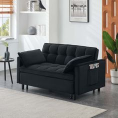 a black couch sitting on top of a rug in a living room next to a potted plant