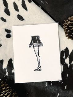 a black and white image of a lamp on a cow print blanket with pine cones