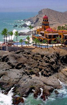 an aerial view of a hotel on the coast with waves crashing in front of it