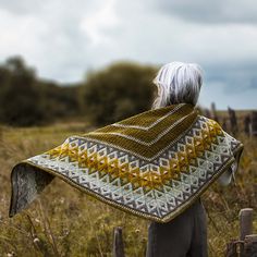 a woman standing in a field with a yellow and white blanket on her back,