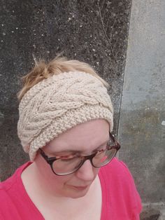 a woman wearing glasses and a knitted headband looking down at her cell phone