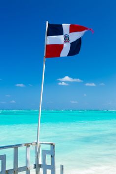 a flag is flying on the beach next to the blue water and clear ocean waters