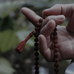 a person holding rosary beads in their left hand and wearing a red tassel on the end