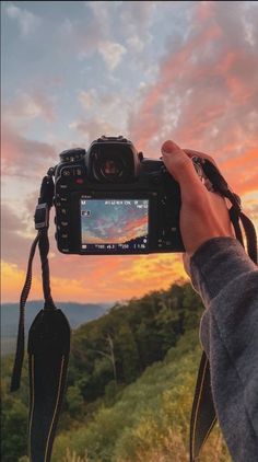 a person holding up a camera with the sun setting in the background