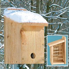 a wooden birdhouse with snow on top and trees in the back ground behind it