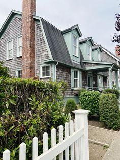 a large house with many windows next to a white picket fence and shrubbery in front of it