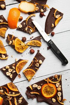 sliced oranges, almonds and chocolate on a white wooden table with a knife