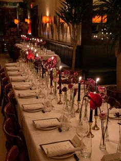 a long table is set with place settings and candles in vases on the tables